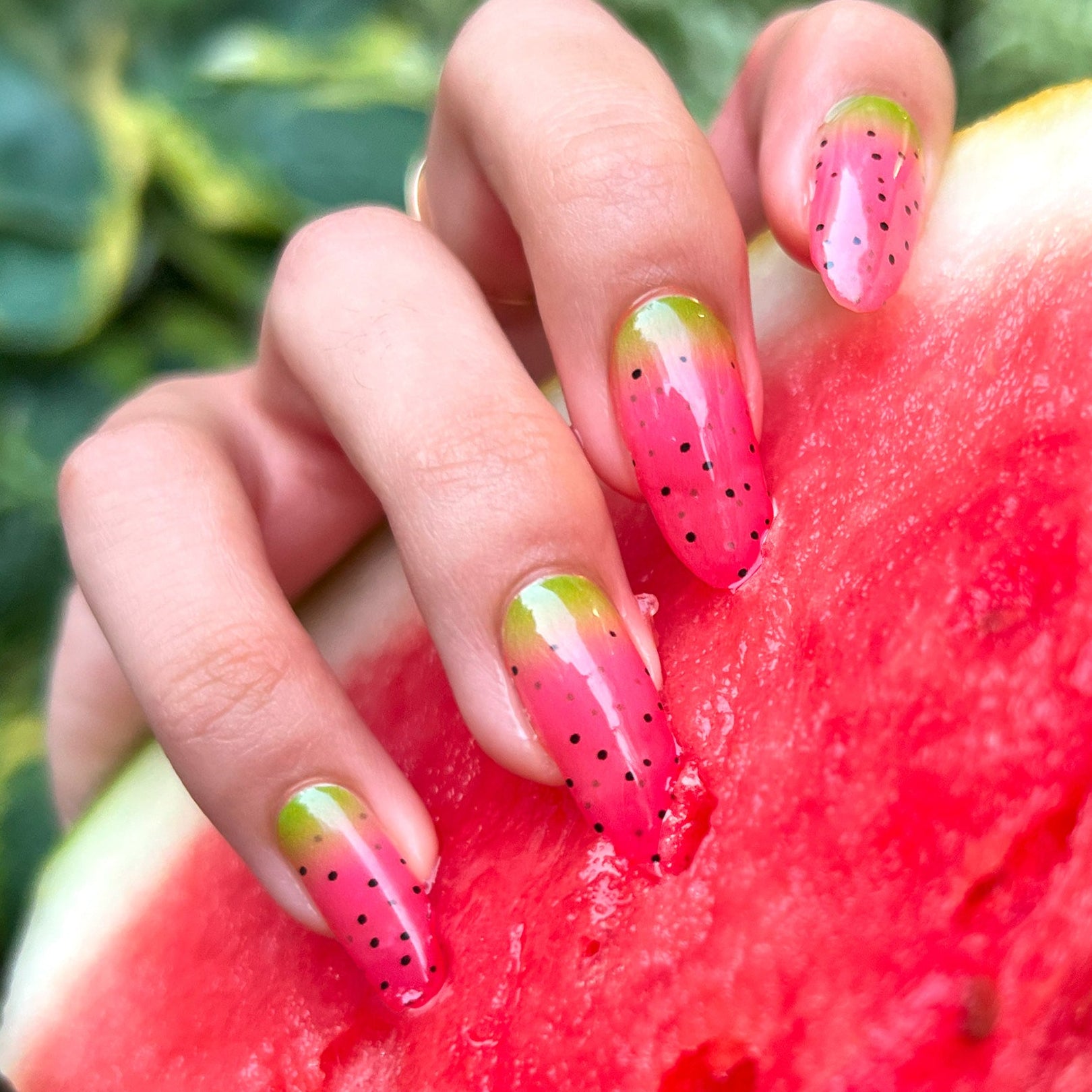 Hand with watermelon-themed nail art holding a slice of watermelon.